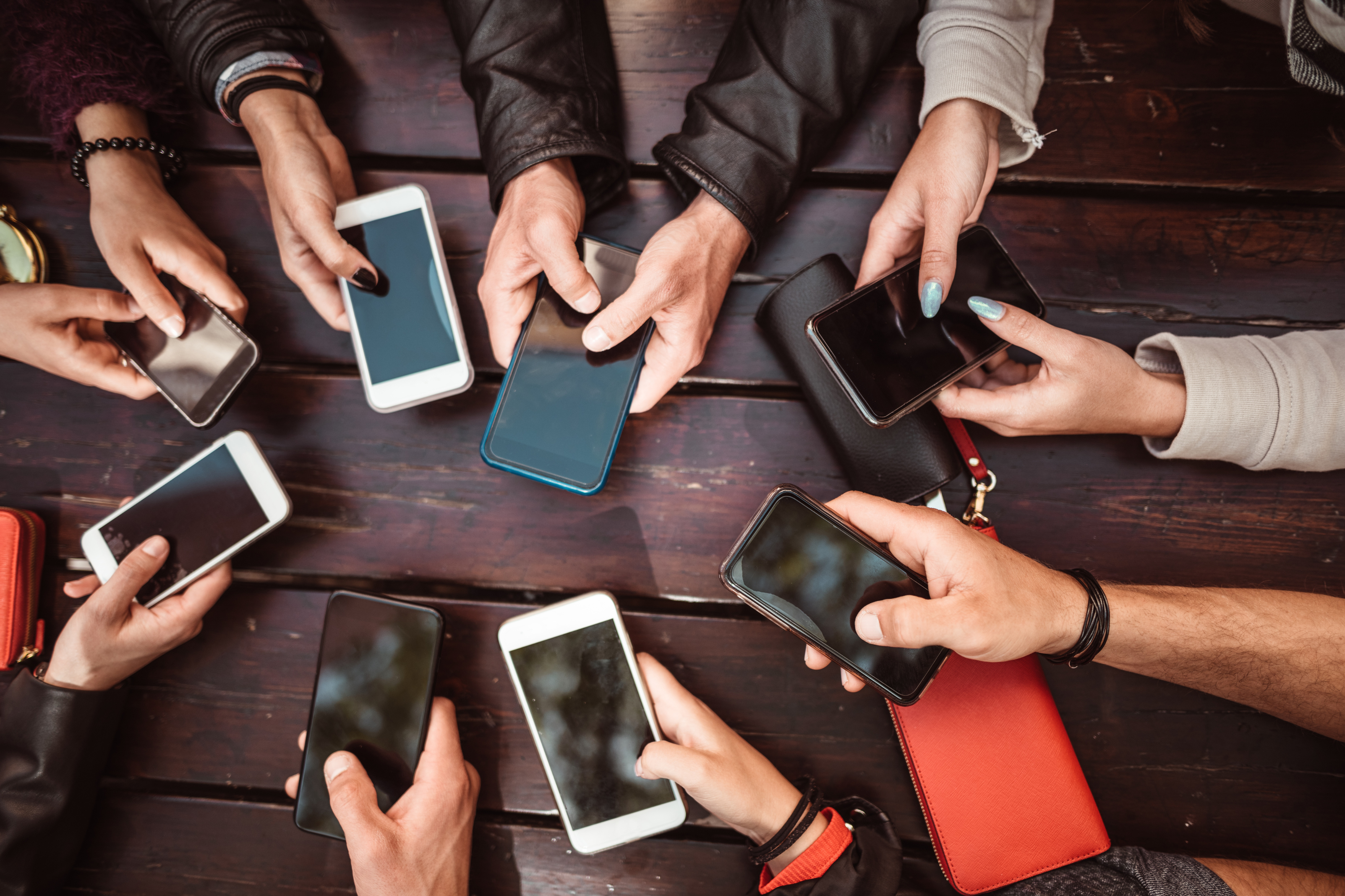 several teenagers sitting around in a circle holding their phones out showing the effect of social media on teenagers