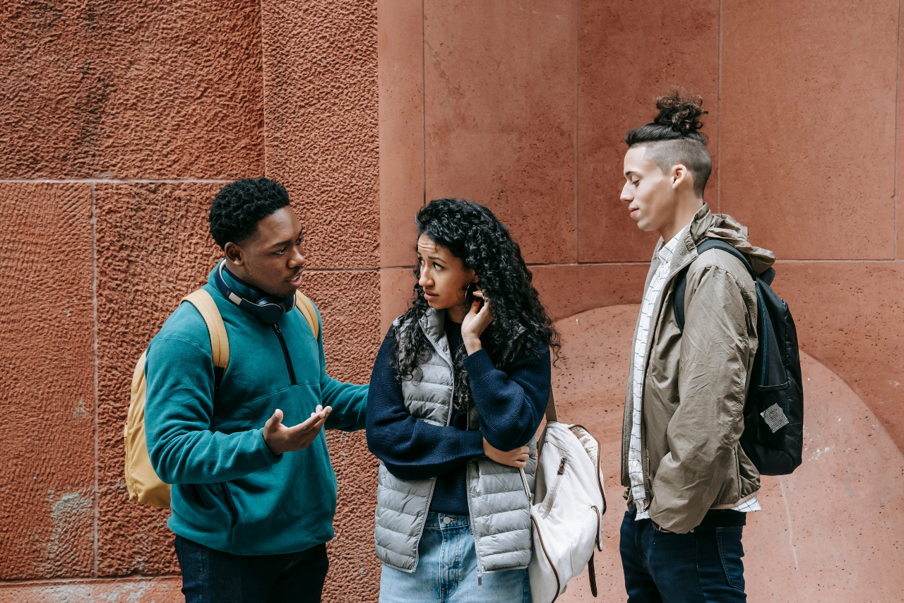 three teenagers standing outside of school showing signs of risky behavior in adolescence