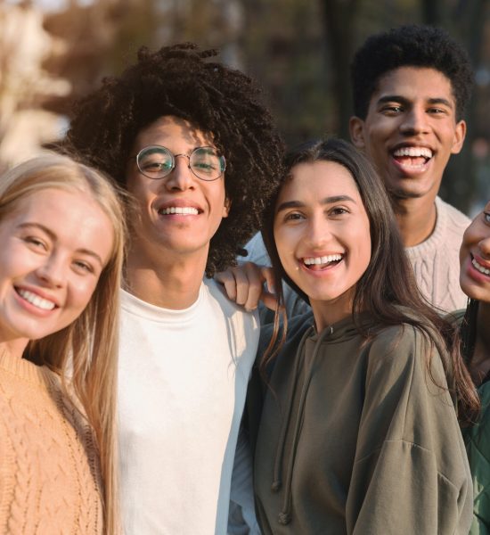 Positive international teen friends taking selfie while walking in autumn park